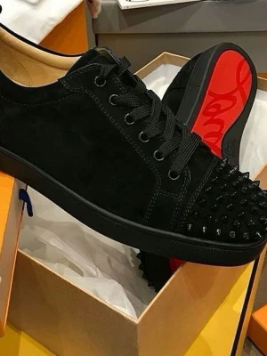 Christian Louboutin svarta sneakers med nitar - Svarta sneakers från Christian Louboutin i mocka med klassisk röd sula och svarta nitar på tån. Skorna har snörning och rund tå, samt platt sula. Perfekt för dig som vill sticka ut med en lyxig och edgy stil. FINNS I STORLEK 41-44