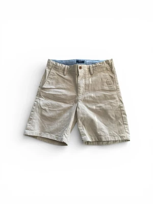 Beige bomullsshorts från GANT - Snygga beige shorts från GANT i mjuk bomull med klassisk passform och midwaist. De har fickor fram och bak, bälteshällor och stängs med knapp och dragkedja. Perfekta för varma dagar och chill stil.
