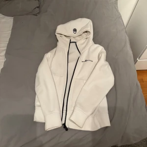 Vit hoodie från Sail Racing med dragkedja - Säljer en fräsch vit hoodie från Sail Racing i storlek 160. Tröjan har hel dragkedja, huva med tryckt logga och två fickor framtill. Materialet är mjukt och är perfekt för kyliga dagar. Snygga svarta detaljer vid dragkedjan. Finns ej o köpa längre! Går att diskutera pris!