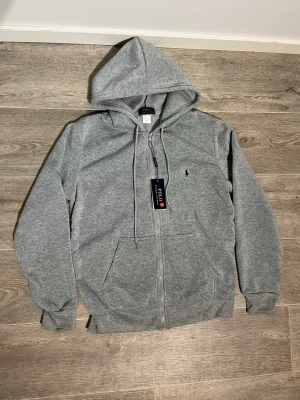 Grå tracksuit från Polo Ralph Lauren - Snygg tracksuit från Ralph lauren tracksuiten är Populär, Skön, Stilig och varm perfekt för kyliga dagar. Den perfekta klädsel om du vill bara chilla 