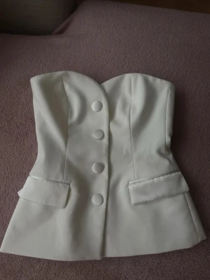 Vit korsett-topp med knappar - Säljer en ” kostymtopp ”  med axelbandslös design och knappar framtill som går att öppna.  Den är ifrån Zara och är slutsåld. Helt ny.