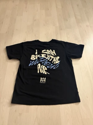 Marcus & Martinus svart t-shirt Youth L - Svart t-shirt från Marcus & Martinus i 100% bomull. Framsidan har ett coolt tryck i beige och blått med ordet 'AIR', och baksidan har texten 'I CAN BREATHE WITHOUT AIR' i samma färger. Klassisk passform och korta ärmar.