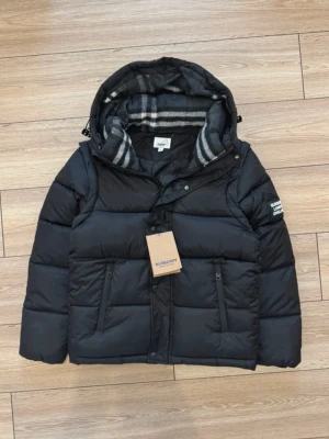 Svart Burberry dunjacka passar L/M - Säljer svart Burberry dunjacka med rutigt foder. Riktigt varm och clean 🔥 Dragkedjor på fickorna och fet Burberry-patch på ärmen. Passa på grabbar, sjuk stil 🖤❄️