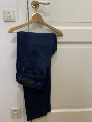 Mörkblå Lee jeans - Snygga mörkblå jeans från Lee med klassisk rak passform och stilren design. Jeansen har en enkel bakficka och svart Lee-lapp vid midjan. Perfekta för dig som gillar tidlös denim och vill ha ett par jeans som funkar till allt. Riktigt snygga!