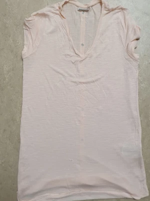 T-shirt - Ljusrosa t-shirt från Noisy May i mjuk bomull. Modellen är ärmlös med v-ringad hals och har dekorativa knappar längs hela ryggen. Perfekt för dig som gillar enkla och stilrena plagg med en twist. Passar dig som vill ha en chill och snygg look.