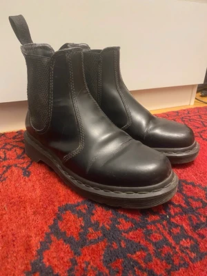 Svarta Chelsea boots Dr. Martens - Säljer ett par klassiska svarta Chelsea boots från Dr. Martens, modell 2976 Mono. Skorna är i fakeskinn med elastiska paneler på sidorna och grov sula. Perfekta för dig som vill ha en tidlös och edgy look. Finns tecken på slitage som syns på bilderna, därav något lägre pris. Fortfarande väldigt fint helhetsintryck. 