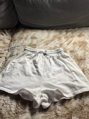 Vita mjuka shorts med snörning - Säljer ett par vita, mjuka shorts med elastisk midja och snörning framtill. De har en avslappnad passform och är perfekta för varma dagar eller chill hemma. Materialet känns som bomull och shortsen har en enkel, stilren look utan mönster eller extra detaljer.