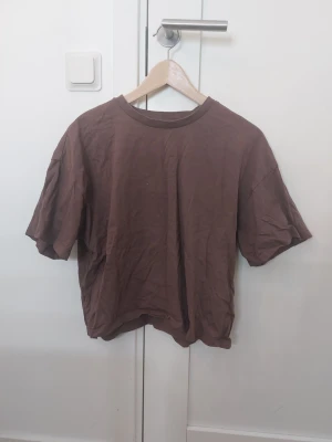 Brun t-shirt från Bik Bok - En basic cropped t-shirt från Bik Bok i mjuk bomull. Modellen har korta ärmar och rund halsringning. Perfekt till jeans eller shorts för en enkel och avslappnad look.