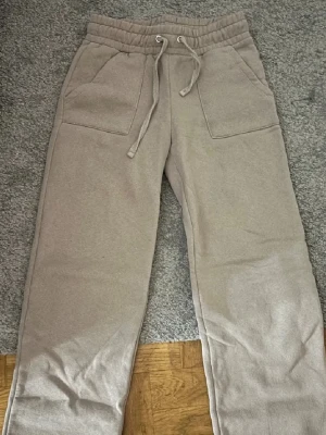 Beige mjukisbyxor Strl S - Beiga mjukisbyxor från 157 i storlek S. Byxorna har bred resår i midjan med snörning, stora fickor fram och raka ben. Tillverkade i mjukt material som känns skönt mot huden. Perfekta för chill dagar eller när du vill vara extra bekväm.