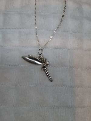 Silverfärgat halsband med fe-berlock - Säljer ett tunt silverfärgat halsband med en detaljrik fe-berlock. Kedjan har justerbar längd och smal länkdesign. Perfekt accessoar för dig som gillar magiska detaljer och vill sticka ut lite extra.