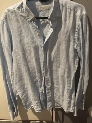 Ljusblå linneskjorta John Henric - Säljer en stilren ljusblå linneskjorta från John Henric i luftig linne. Skjortan har klassisk krage, knappar framtill och långa ärmar. Perfekt för dig som gillar en clean och avslappnad look. Passar bra till kommande vår och sommar, storlek 37 motsvarar typ S