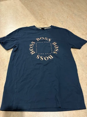 Mörkblå t-shirt från Hugo Boss - Snygg mörkblå t-shirt från Hugo Boss med rund hals och tryck i form av BOSS-loggan i en cirkel på bröstet. Perfekt för en clean och stilren look.
