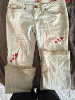 Ljusblå jeans med röda hjärtan - Säljer ett par ljusblå jeans från No Boundaries som jag köpte second hand i London, med unika röda hjärtan som jag målat dit själv på båda benen. Jeansen har klassisk femficksdesign, raka ben och är tillverkade i bomull med lite stretch för extra komfort. Perfekta för dig som vill sticka ut med en personlig touch.
