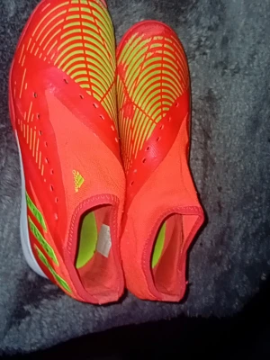 Röda och gula adidas fotbollsskor - Säljer ett par adidas fotbollsskor futsal i rött och gult med coolt grafiskt mönster och elastisk ovandel. Skorna har en strumpliknande passform och är perfekta för dig som vill sticka ut på planen. Adidas-logga på sidan och klassiska ränder i neonfärg. Preditors också.