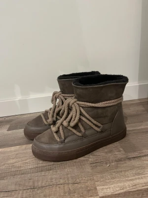 Beigea Inuikii - Säljer ett par beige skor från Inuikii med mjuk pälsfodring. Skorna är i mocka och skinn, har rund tå och platt sula. Perfekta för kalla dagar med sin varma insida och snygga design. Använda en gång, pga för små. 