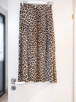 Leopardmönstrad kjol - Säljer en kjol med leopardmönster i beige, svart och bruna toner. Kjolen har en lätt utsvängd passform och är tillverkad i ett mjukt, följsamt material som ger snyggt fall. Perfekt statement-plagg för dig som vill sticka ut.