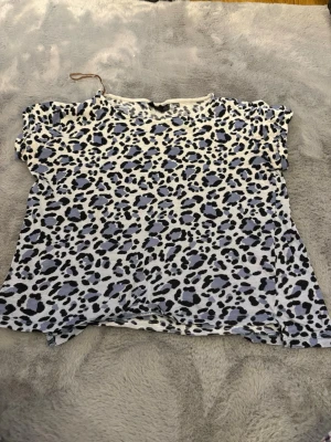 Leopardmönstrad t-shirt KappAhl - Säljer en kortärmad t-shirt från KappAhl med grymt leopardmönster i svart och gråblått på vit botten. Skön passform och mjukt material, perfekt till jeans eller shorts för en cool look.