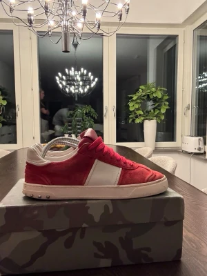Valentino Rockrunner röda sneakers - Riktigt snygga Valentino Rockrunner sneakers i rött mocka med vita detaljer och vita partier på sidan. Skorna har röda skosnören, platt sula och coola nitar baktill på sulan. Perfekta för dig som vill sticka ut med en exklusiv streetstil.