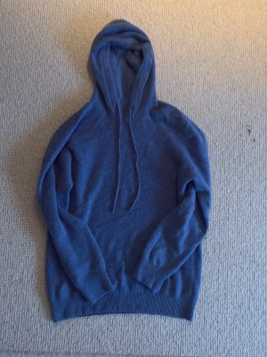 Blå stickad hoodie - Mellanblå stickad hoodie med luva och snören. Storlek XS liten i storleken. Inga tecken på användning. Perfekt nu till vintern då den är lite tjockare. Bara att fråga vid frågor eller ge förslag på pris.