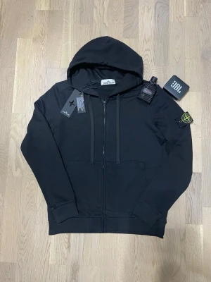 Svart Stone Island - Zip Hoodie  - Stilren och ikonisk Stone Island zip-hoodie i klassisk svart färg. Ett premiumplagg med hög kvalitet och tidlös design, utrustad med den välkända avtagbara Stone Island-kompassen på ärmen.  • Märke: Stone Island • Typ: Zip-hoodie • Färg: Svart • Passform: S-M • Skick: Mycket fint skick • Avtagbar ikonisk Stone Island-badge på ärmen • Mjuk, tung och högkvalitativ kvalitet  En riktig garderobsfavorit som håller både stil och värde över tid.  🔹 Hög efterfrågan 🔹 Begränsat utbud 🔹 Först till kvarn