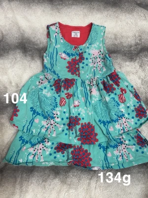 Turkos blommig klänning Polarn o pyret  - Superfin turkos klänning från Polarn o pyret med färgglatt blommigt mönster. Ärmlös modell med knappar framtill och utställd kjol. Perfekt för dig som gillar lekfulla och glada färger!🌸 Fint använt skick. Storlek 104