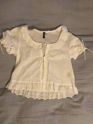 Vit blus med spets och volang  - Supersöt vit blus  med korta puffärmar, spetsdetaljer vid krage och nederkant samt volang. Har aldrig använt den, köpt i Norge. //skriv om ni undrar om något 💕(läs min profil)