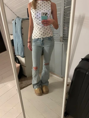Ljusblå bootcut jeans  - Säljer ett par ljusblå bootcut jeans med slitna knän och slitna benslut. Jeansen har låg midja och klassisk femficksmodell. På bakfickorna finns broderade detaljer i rosa. Perfekta för en avslappnad och trendig look.