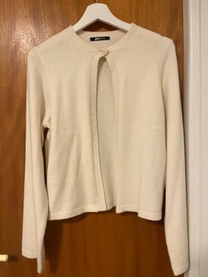 Beige kofta från Gina Tricot - Säljer en stilren beige kofta från Gina Tricot i mjukt stickat material. Koftan har rund halsringning, lång ärm och stängs med en enkel knapp upptill. Perfekt att slänga över en topp för en clean look. Har aldrig använt 