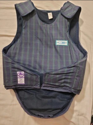 Rutig skyddsväst från Airowear - Säljer en rutig skyddsväst från Airowear i mörkblått och grönt med meshfoder. Västen har kardborreknäppning vid axlar och midja samt BETA-certifiering. Perfekt för ridning och ger bra skydd vid aktiviteter till häst.