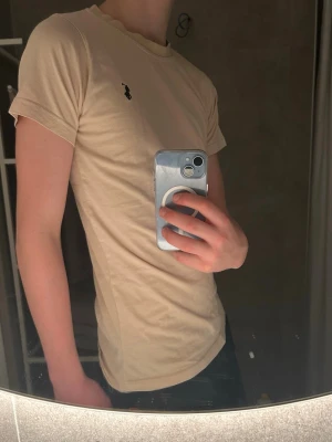Beige t-shirt från U.S. Polo Assn. - Säljer en beige t-shirt från U.S. Polo Assn. i storlek S. T-shirten har korta ärmar, rund halsringning och en liten svart logga broderad på bröstet. Tillverkad i mjuk bomull för en skön känsla och sitter tight mot kroppen.