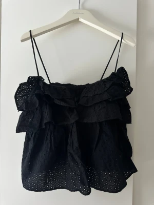 Svart volangig linnetopp från Zara - Supersöt svart linnetopp från Zara med tunna axelband, broderade hål och flera volanglager. 