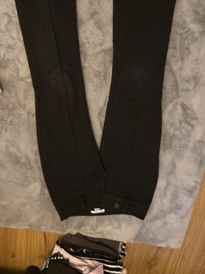 Svarta byxor från Gina Tricot - Säljer ett par svarta byxor från Gina Tricot i storlek 152. Byxorna har raka ben, två stora knappar framtill och är tillverkade i ett mjukt tyg som känns bekvämt. Perfekta till en clean och enkel look. Som ni kan se också så har de små små hål där bak men det är inget man tänker på🤍