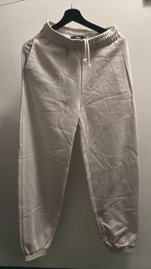 Beiga mjukisbyxor från Bik Bok - Säljer ett par beiga mjukisbyxor från Bik Bok med resår och snörning i midjan. Byxorna har avslappnad passform, muddar vid bensluten och är tillverkade i mjukt bomullsmaterial. 