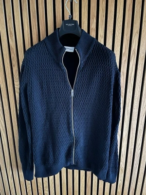 Mörkblå kofta från Lindbergh White - Säljer en mörkblå kofta från Lindbergh White med grovstickad struktur och hel dragkedja framtill. 