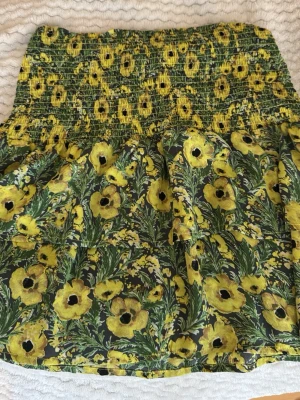Blommig kjol - Supersöt kjol från Holly & Whyte by Lindex i storlek S. Kjolen har ett gult blommönster på mörk botten och smock i midjan för en bekväm passform. Perfekt för dig som vill ha en färgglad och somrig vibe.