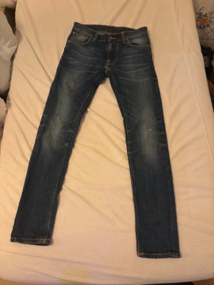 Nudie Jeans Skinny Jeans 28/32 - Mörkblå skinny jeans från Nudie Jeans i storlek 28/32. Klassisk femficksmodell med orange sömmar och slitningar på benen för en cool look. Tillverkade i mjukt jeansmaterial som sitter tight hela vägen ner.