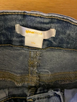 Blå jeans från Gina Tricot, storlek 164 - Säljer ett par klassiska blå jeans från Gina Tricot i storlek 164. Jeansen har fem fickor, bälteshällor och en snygg tvättad look. De är bootcut i modellen och har normal passform, perfekta till vardagsstilen.