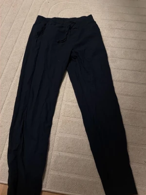 Svarta mjukisbyxor med snörning - Säljer ett par svarta linnebyxor med dragsko i midjan och raka ben. Byxorna har en enkel och clean look, perfekta för chill dagar eller när du vill vara bekväm. Tillverkade i mjukt material och har fickor på sidorna.