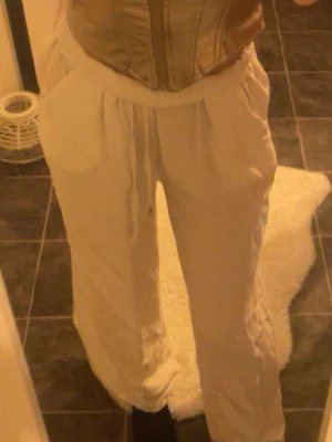  Vita linnebyxor  - Säljer ett par vita linnebyxor med avslappnad passform och snörning i midjan. Byxorna har resår i midjan och är tillverkade i ett mjukt bomullsmaterial. Perfekta för chill dagar eller när du vill vara extra bekväm.