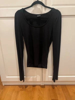 Svart långärmad topp med slits - En svart långärmad topp från Gina Tricot med rund halsringning och smal passform. Ärmarna har en snygg slitsdetalj vid ärmslutet som ger en extra touch. Perfekt att styla med jeans eller kjol.