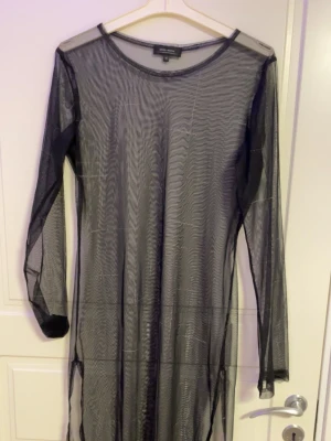 Svart meshklänning med lång ärm - Transparent svart meshklänning från Monki med lång ärm och rund halsringning. Klänningen har en rak passform och är perfekt för lager på lager-stil. Tunn och luftig, vilket ger en edgy vibe.