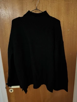 Svart oversized stickad polotröja - Säljer en svart oversized stickad polotröja med hög krage. Tröjan har en lös passform och långa ärmar, perfekt för lager-på-lager-stil. Enkel och stilren design som passar till det mesta. Materialet känns mjukt och bekvämt.