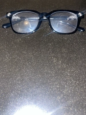 Svart glasögonbåge med soprankors - Säljer ett par svarta exklusiva chrome bluelight glasögon med rektangulär form och silvriga soprankors-detaljer på skalmarna. Bågarna har en clean och stilren look som passar till det mesta. Perfekt accessoar för dig som vill sticka ut lite extra. Pris går att diskuteras.