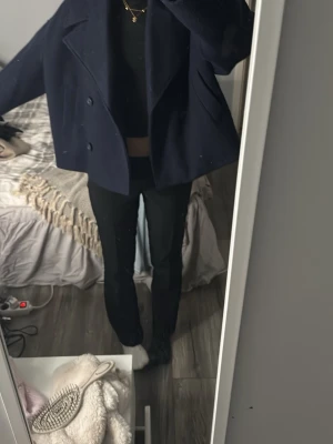 Mörkblå kort skepparkavaj i ull - Kort skepparkavaj i mörkblått med dubbelknäppning och bred krage. Jackan har en loose passform och är tillverkad i ull, perfekt för kyligare dagar. Snygg och stilren modell som passar till det mesta.