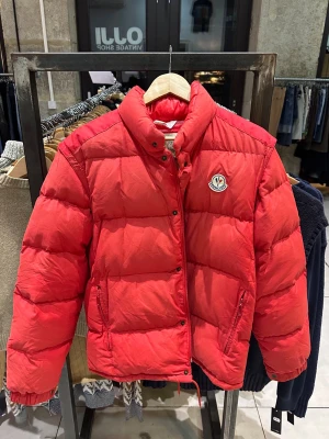 Vintage Moncler dunjacka - Snygg röd dunjacka från Moncler med klassisk pufferdesign. Jackan har har avtagbara ärmar vilket gör att den dubblar som väst. Perfekt för kalla dagar och för dig som vill ha ett unikt plagg. Köpt från en vintagebutik i Lyon.