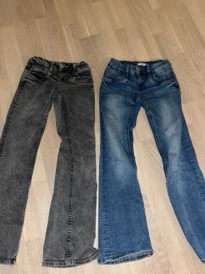 Bootcut jeans från Gina Tricot, två färger - Två par bootcut jeans från Gina Tricot i storlek 152. Ena paret är svartgrått och det andra är klassiskt blått med slitningar. Båda har normal passform, fem fickor och är tillverkade i mjukt bomullsjeansmaterial. Använd fåtal gånger.