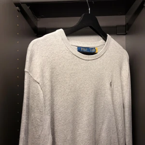 Ljusgrå stickad tröja Polo Ralph Lauren - Snygg ljusgrå stickad tröja från Polo Ralph Lauren med rund halsringning och diskret broderad logga på bröstet. Tröjan har en klassisk passform och ribbade muddar vid ärmslut och nederkant. Perfekt till jeans. Xs, men passar även small