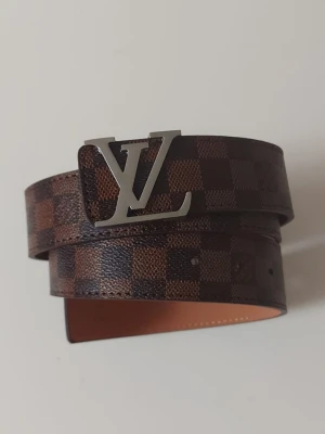 L bälte rutig 115cm - Helt nytt brunt bälte. Aldrig använt, i perfekt skick. Längd: 115 cm. Klassisk design, se bilder för detaljer.