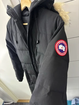 Svart dunjacka från Canada Goose - Säljer en svart dunjacka från Canada Goose. Jackan har dragkedja, knappar och två stora fickor framtill. Klassisk patch. Den är äkta, S men skulle kunna passa som M. Perfekt för kalla vinterdagar. Kom gärna med förslag om pris 😊