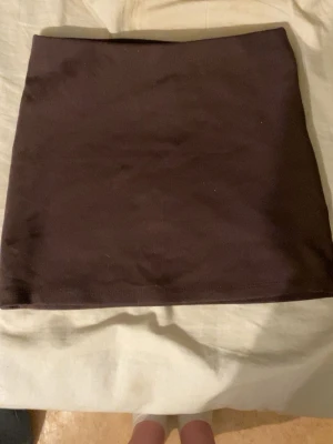 Mörkbrun minikjol Aleyna XS - Enkel och stilren mörkbrun minikjol från Aleyna. Kjolen har en rak passform och är tillverkad i ett mjukt material som känns bekvämt mot huden. Perfekt att matcha med en crop top eller oversized tröja för en trendig look.